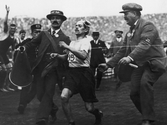 Dorando Pietri of Italy, on the verge of collapse, is helped across the finish line in the Marathon event of the Olympic Games in London, 1908. He was subsequently disqualified. (Credit: Public Domain)