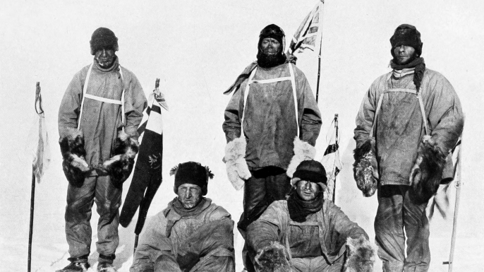 Robert Falcon Scott's Pole party of his ill-fated expedition, from left to right at the Pole: Oates (standing), Bowers (sitting), Scott (standing in front of Union Jack flag on pole), Wilson (sitting), Evans (standing). Bowers took this photograph, using a piece of string to operate the camera shutter. (Credit: Public Domain)