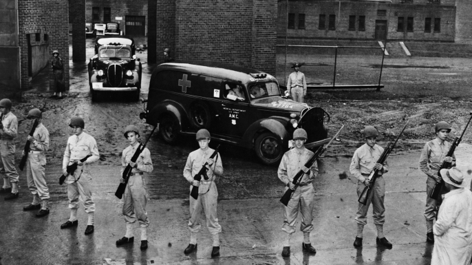 Armed soldiers guard the ambulances carrying the bodies of six executed Nazi saboteurs.