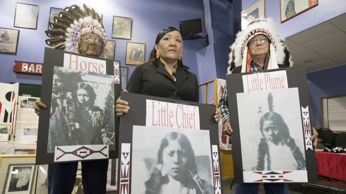 Yufna Soldier Wolf, center, of the Northern Arapaho, with tribal elders, Mark Soldier Wolf and Crawford White Sr., holds pictures of the three Arapaho children buried at the Carlisle Indian School. Experts made final preparations August 7, 2017, to exhume bodies of three Native American children named Little Plume, Horse and Little Chief who died about 135 years ago while attending a government-run school in Pennsylvania, and return the bodies to Wyoming. (Credit: Charles Fox/The Philadelphia Inquirer/AP Photo)
