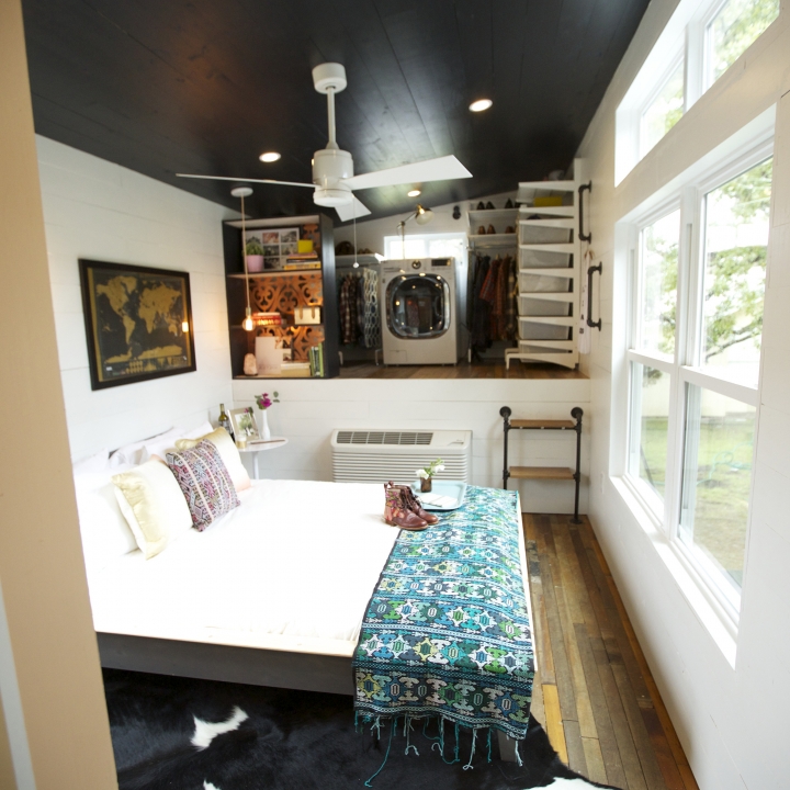An open bedroom space with an open closet and dual washer/dryer shows that this couple doesn't have to sacrifice utility for tiny living.
