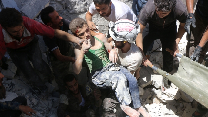 The White Helmets carry a young boy after they dug him out from under the rubble of buildings destroyed following reported air strikes on the rebel-held neighborhood of Al-Mashhad in the northern city of Aleppo, on July 25, 2016. (Credit: THAER MOHAMMED/AFP/Getty Images)
