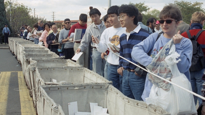 People placing visa applications in bins outside the Merrifield, Virginia post office in hopes of receiving one of the 40,000 green cards to be distributed via lottery on a first-come, first-served basis, 1991. (Credit: Robert Brown/AP Photo)