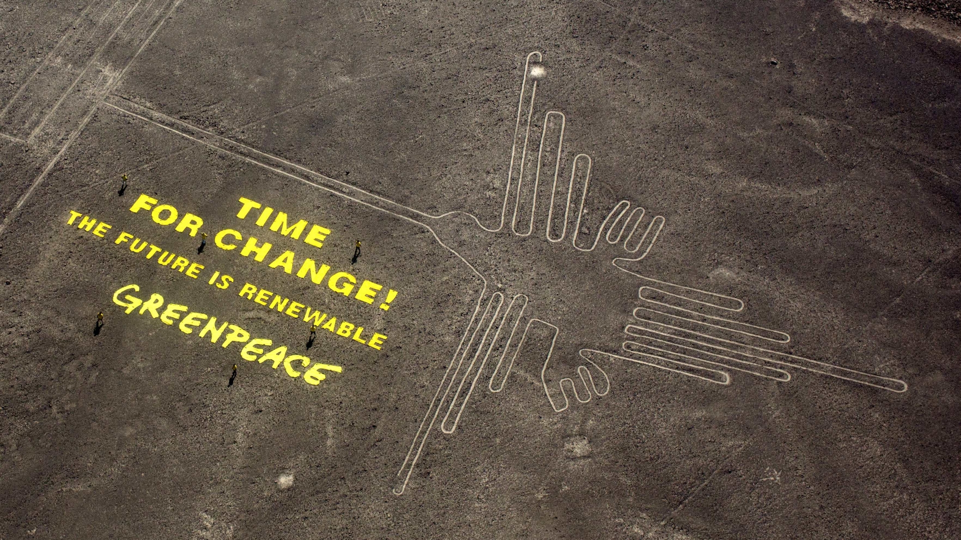 Greenpeace activists standing next to large letters that spell out "Time for Change: The Future is Renewable" next to the hummingbird geoglyph in Nazca, Peru. (Credit:Rodrigo Abd/AP Photo)
