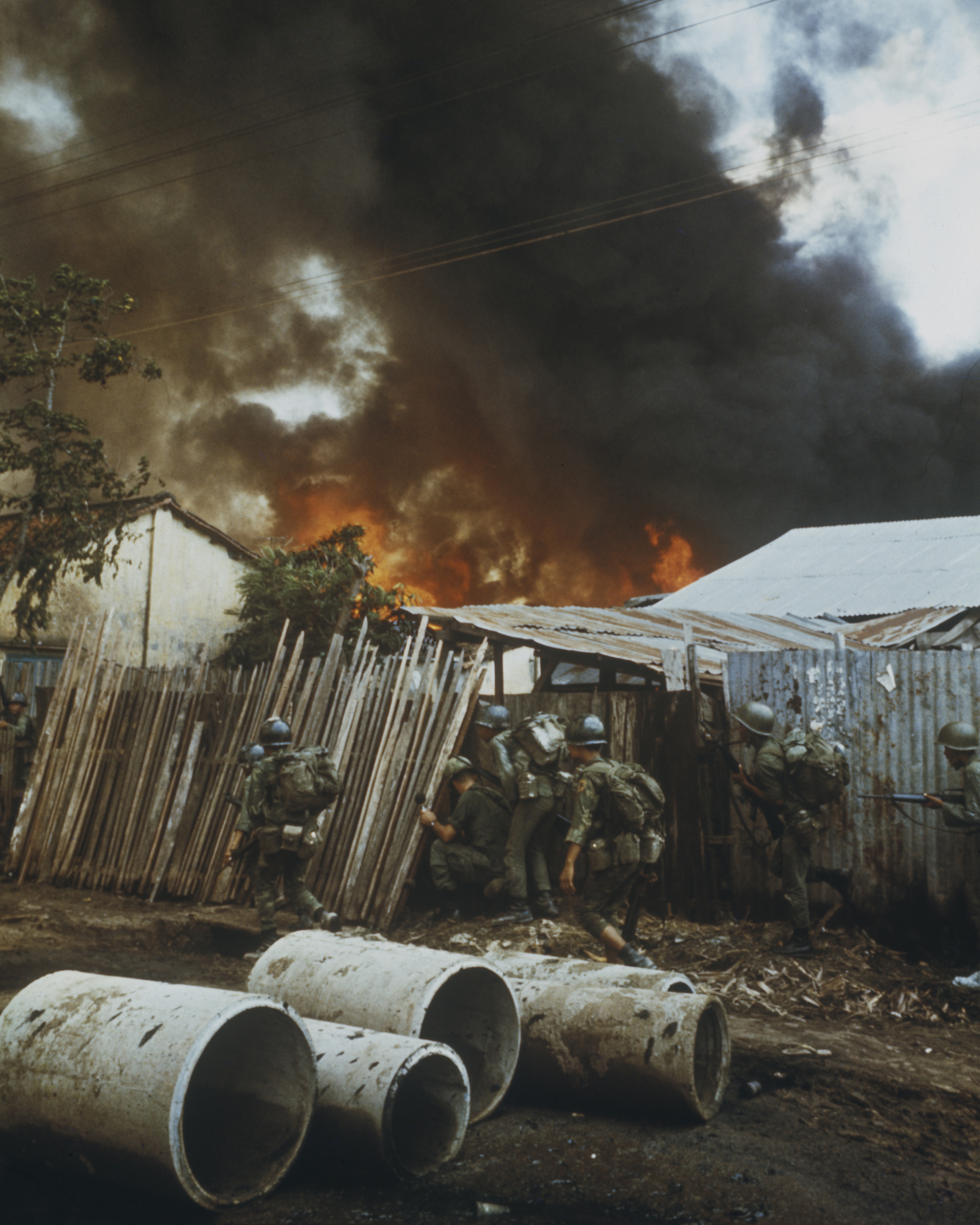 Soldiers taking cover beside a fence as a fire rages among buildings in Saigon during the Tet Offensive. (Credit: Rolls Press/Popperfoto/Getty Images)